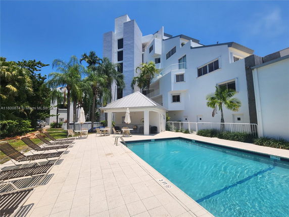Outdoor swimming pool area with lounge chairs and a nearby building.