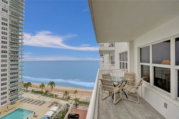 Balcony view overlooking the ocean with a table and chairs, adjacent to high-rise buildings and a beach.
