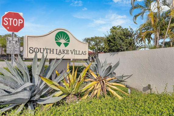 Entrance sign for South Lake Villas with surrounding plants and a stop sign nearby.