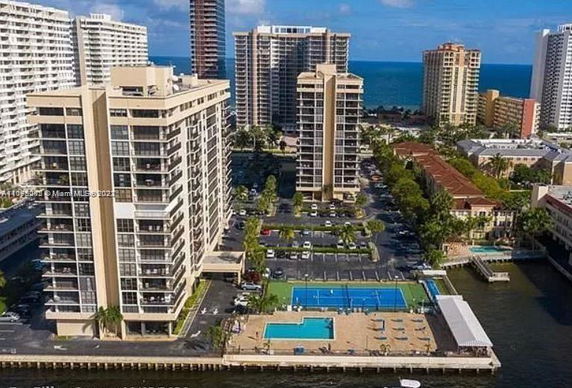 Elevated view of multiple high-rise buildings near a waterfront, with swimming pools and tennis courts in the foreground.