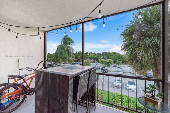 Outdoor balcony with string lights, table and chairs, bicycle, and view of parking area and greenery.