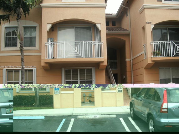 Front view of a multi-story building with balconies and a parking area.
