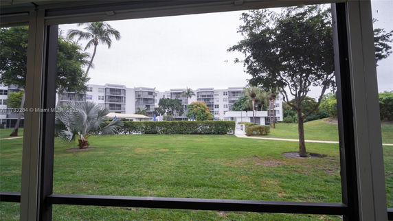 View from indoors looking out at a courtyard with trees and a multi-story building in the background.