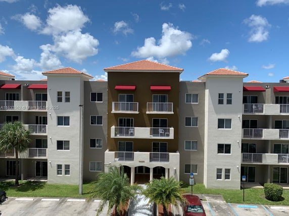 Front view of a multi-story residential building with balconies and red awnings.
