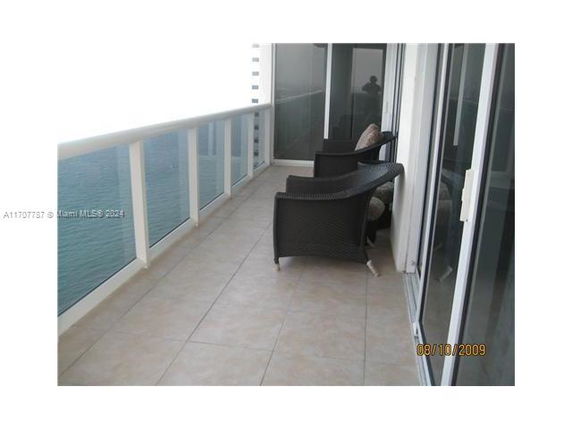 Balcony with glass railing overlooking water, featuring two wicker chairs and a tiled floor.