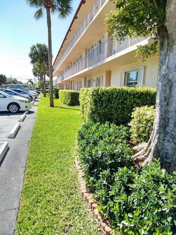 Side view of a multi-story building with balconies and adjacent parking area.