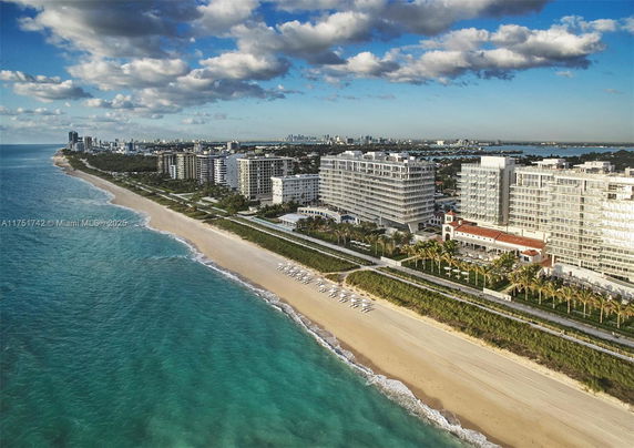 Aerial view of beachfront buildings along a coastline with clear blue water.