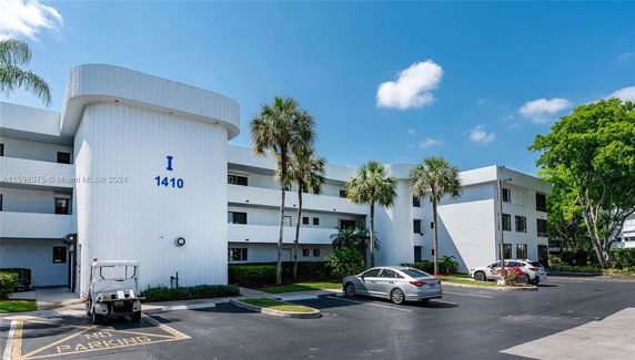 Front view of a multi-story building with palm trees and a parking lot.