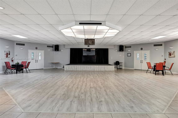 Interior view of a large, open recreational room with a stage and tables with chairs.