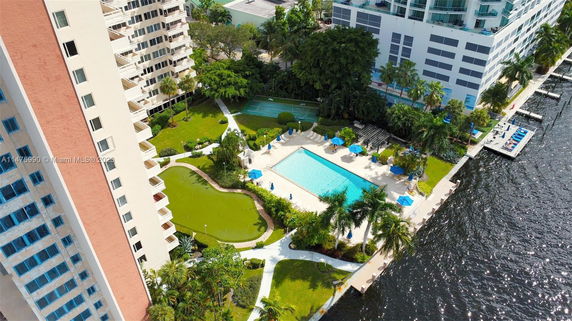 Aerial view of high-rise residential buildings with a pool, walking paths, and waterway.