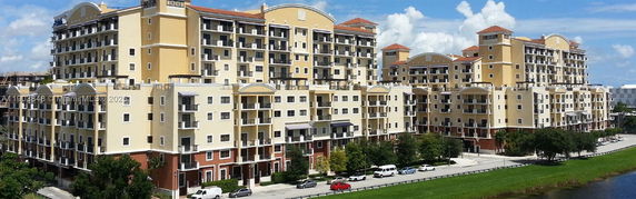 Front view of a multi-story apartment complex with numerous balconies and a row of parked cars.