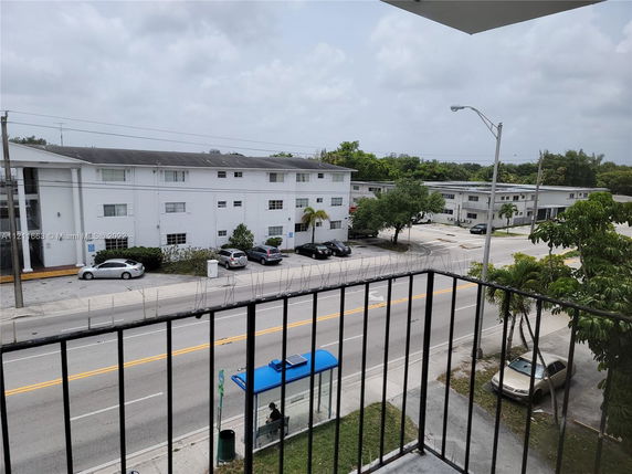 View from a balcony overlooking a street with residential buildings and a bus stop.