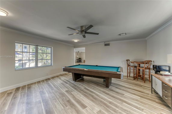 Room with a pool table, wooden flooring, and a window with an outdoor view.