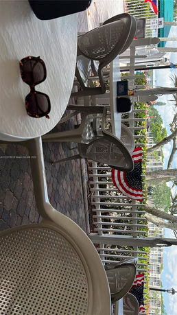 Outdoor seating area with tables and chairs near a railing decorated with a flag.