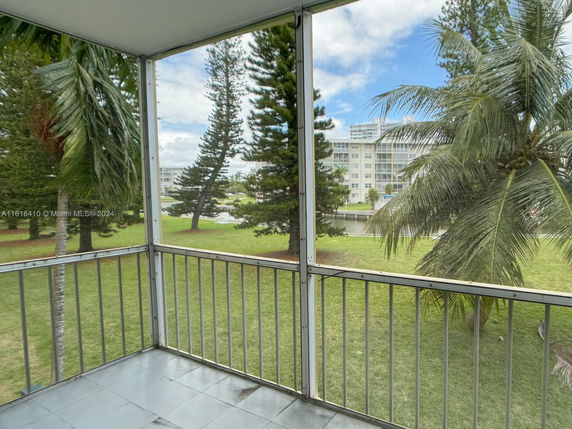 View from a balcony overlooking a grassy area with trees and a distant building.