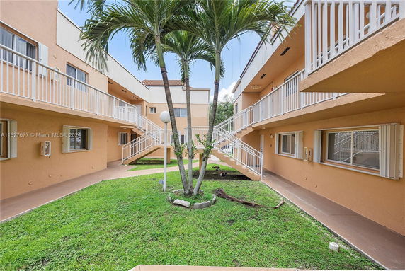 View of a two-story apartment complex courtyard with staircases and green landscaping.