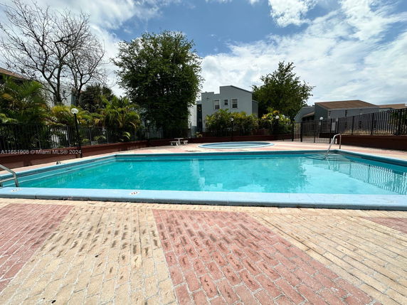 Outdoor swimming pool with a surrounding fenced area and trees.