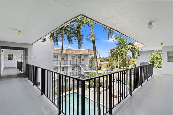 View of apartment buildings with balconies and a swimming pool, surrounded by palm trees.