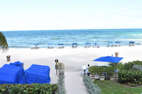View of a sandy beach with blue umbrellas and ocean in the background.