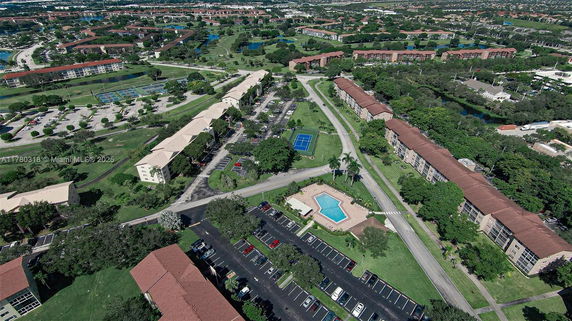 Aerial panoramic view of a residential area with multiple buildings, parking areas, a swimming pool, and tennis courts.