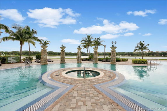 View of an outdoor pool area with stone pillars and palm trees, overlooking a lake.