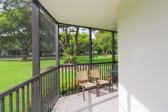 Screened patio with chairs next to a grassy park area with trees.