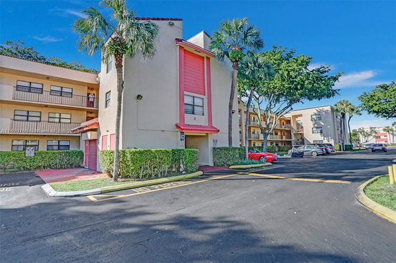 Front view of a multi-story apartment building with balconies and red roofing accents.