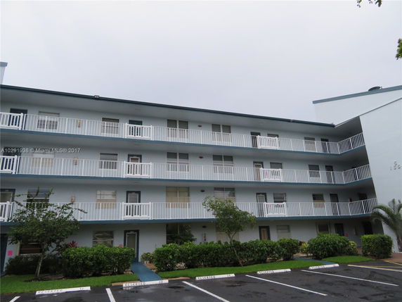Front view of a multi-story residential building with balconies and a parking area.