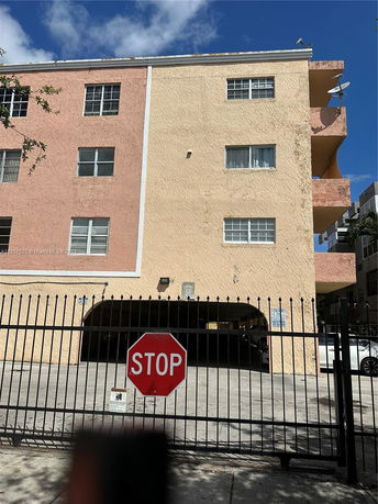 Front view of a multi-story building with a gated entrance and a stop sign.