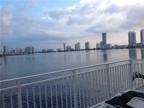 View of high-rise buildings across a body of water from a vantage point with a railing in the foreground.