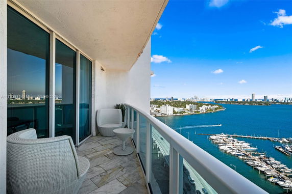 View from a balcony with glass railing overlooking a marina and cityscape across the water.