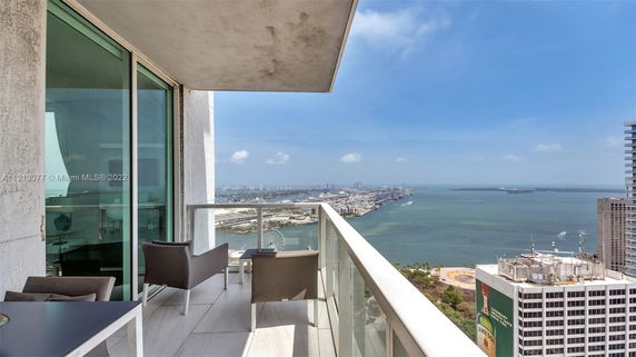Panoramic view from a high-rise building balcony, featuring cityscape and ocean.