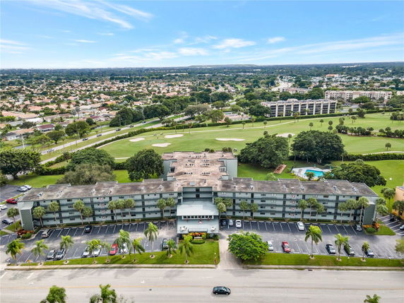 Aerial view of a multi-story apartment building with parking area, surrounded by greenery and a golf course.