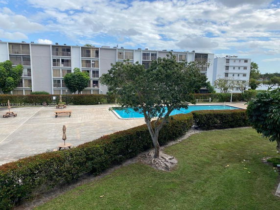 Outdoor view of a swimming pool with surrounding patio area and a multi-story residential building in the background.