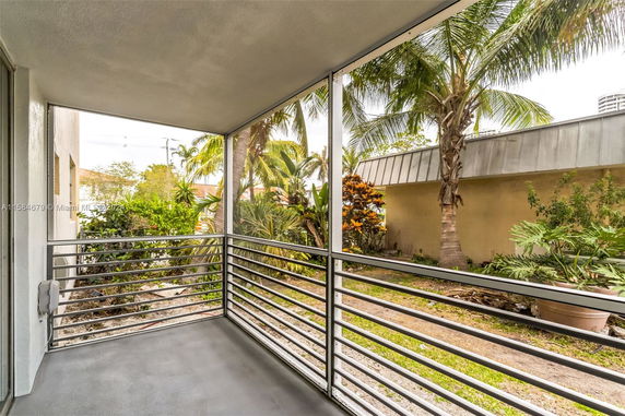 View from a balcony with a metal railing overlooking a garden with palm trees.