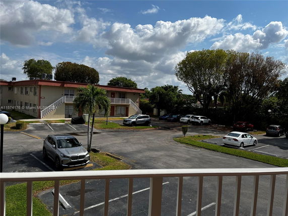 Outdoor parking area with multiple cars and a two-story building in the background.