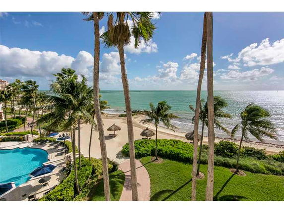 View of a beachfront area with palm trees, a sandy beach, and a pool nearby.