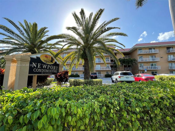 Front view of a condominium building with multiple balconies and palm trees in the foreground.