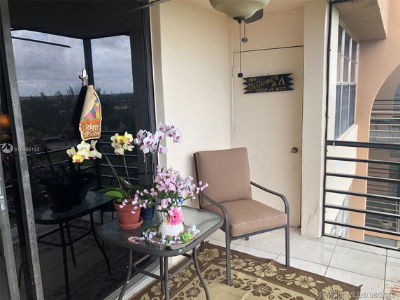 Balcony area with a chair, table, and potted plants. A sliding glass door reflects the view of the surroundings.