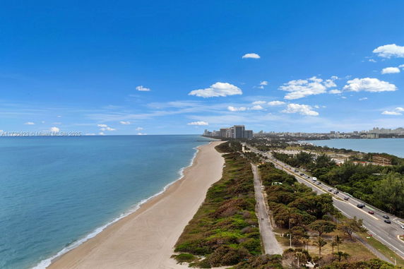 Panoramic view of a coastline with a sandy beach and city skyline in the distance.