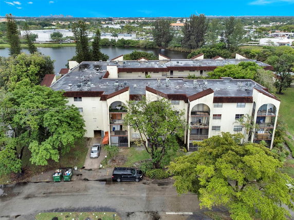 Aerial view of an apartment building surrounded by trees and a body of water in the background.