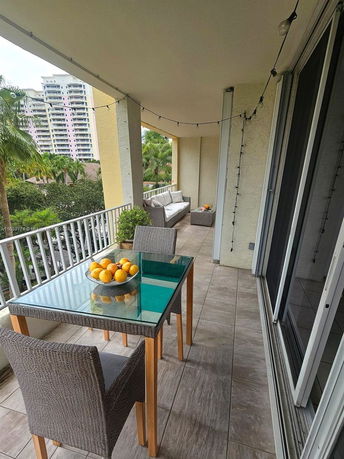 Balcony area with a glass table and wicker chairs, overlooking nearby buildings.