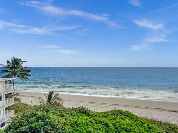 Panoramic view of the ocean from a high vantage point, showing a sandy beach, greenery, and part of a building on the side.