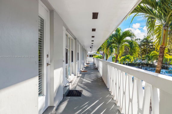 Exterior corridor of a building overlooking palm trees and parked cars.