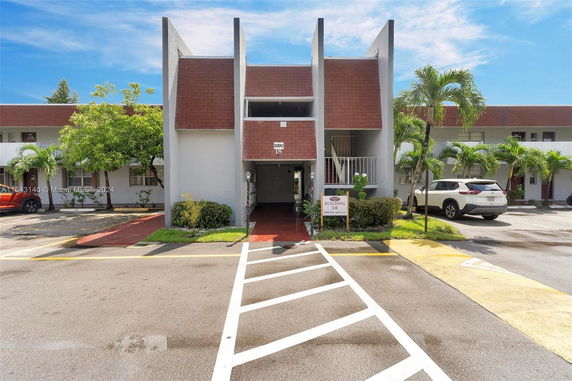 Front view of a multi-story residential building with a sloped roof and parking spaces.
