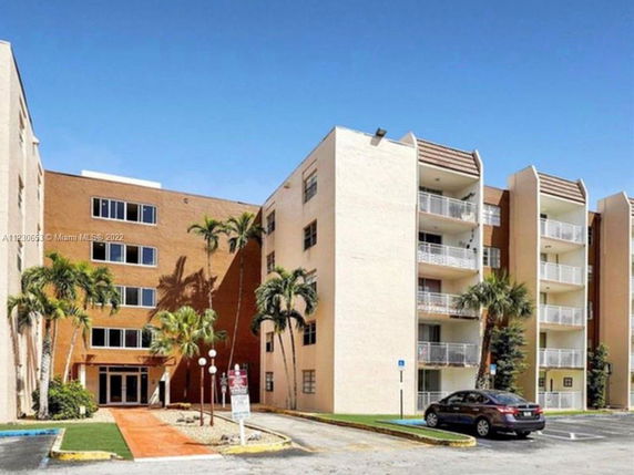 Front view of a multi-story apartment building with balconies and palm trees.