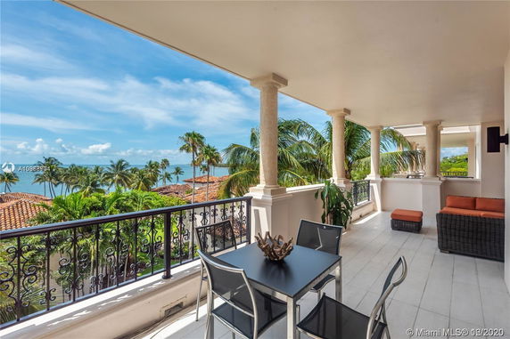 Balcony view featuring palm trees and ocean, with seating and a table.