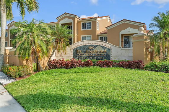 Front view of a condominium building with a decorative sign and landscaping.