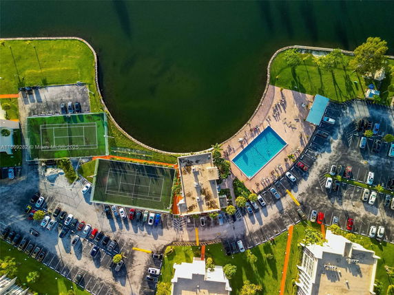 Aerial view showing a swimming pool, tennis courts, parking areas, and adjacent water body.