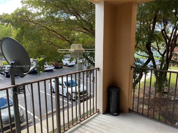 View from a balcony overlooking a parking area with trees in the background.